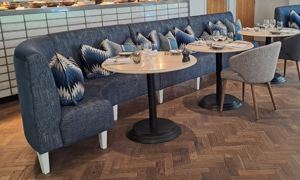 A blue J-shaped banquette with grey tall feet and fixed back and seats.